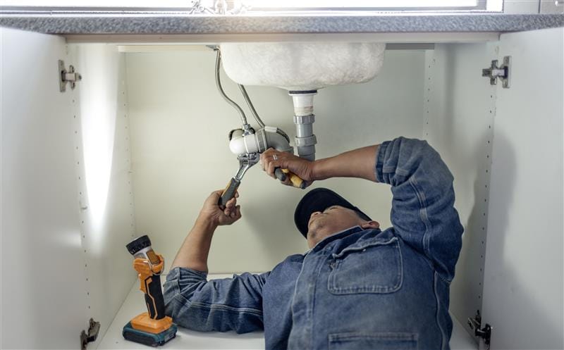 Plumber repairing pipes beneath a bathroom sink in Santa Clarita